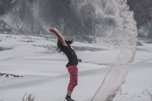 A man joyfully plays by throwing snow in a wintery landscape.