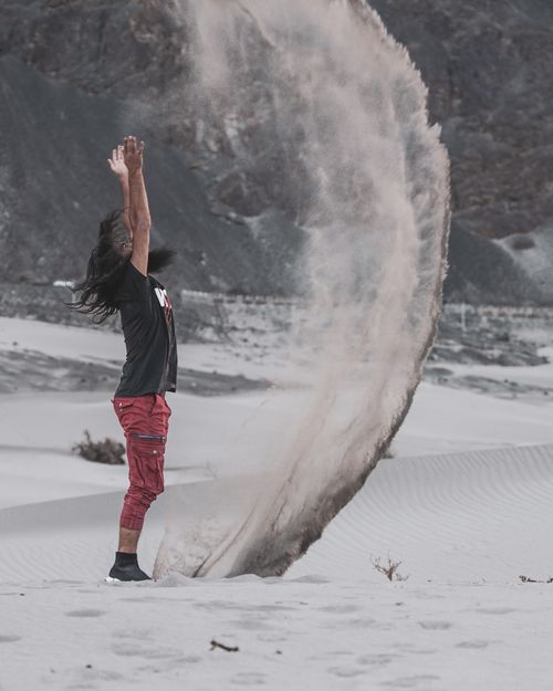 Free Energetic scene of man tossing sand in a vast desert, creating a stunning arc. Stock Photo