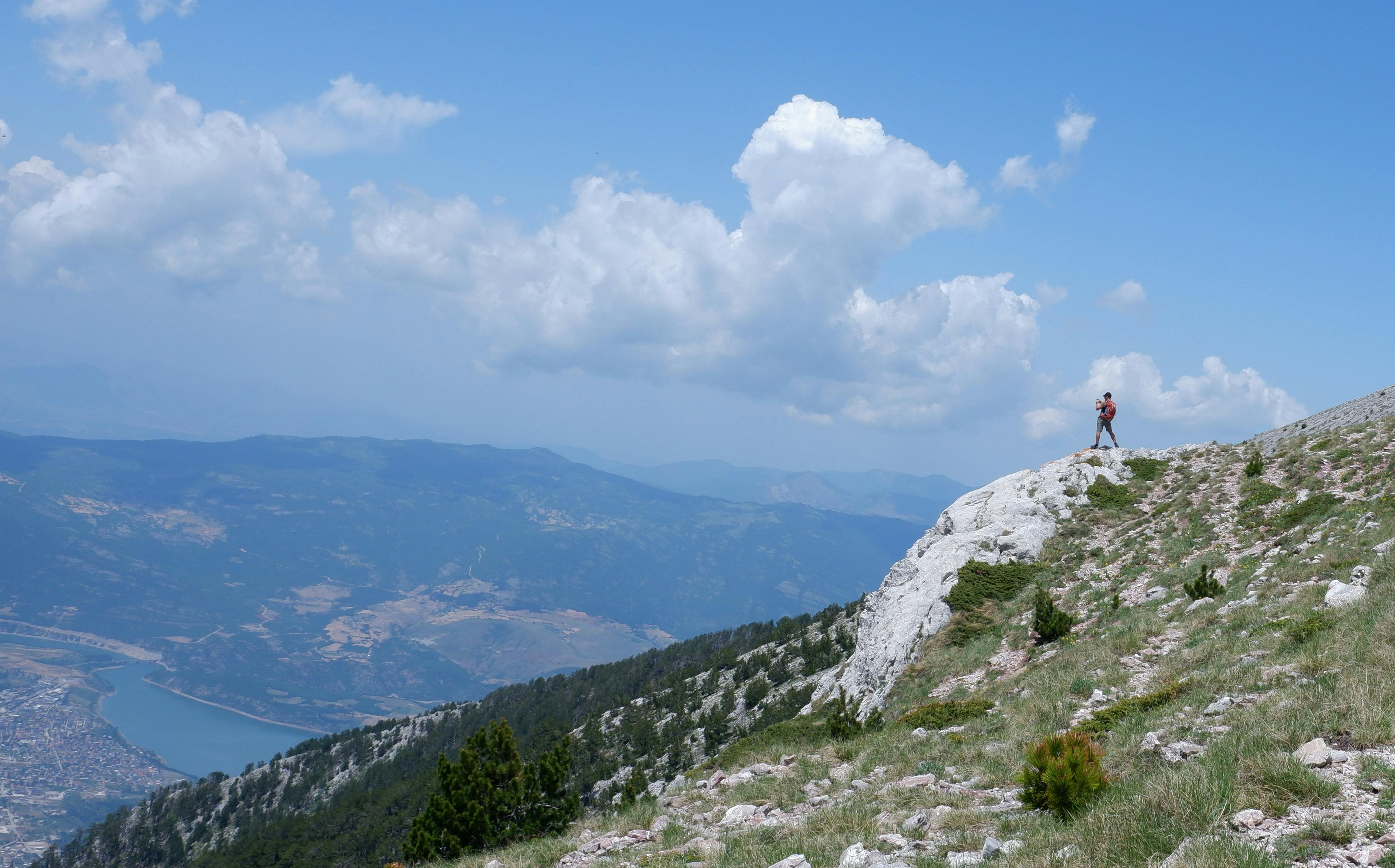 A hiker stands on a rocky mountain ridge, enjoying a breathtaking view of expansive valleys and skies.