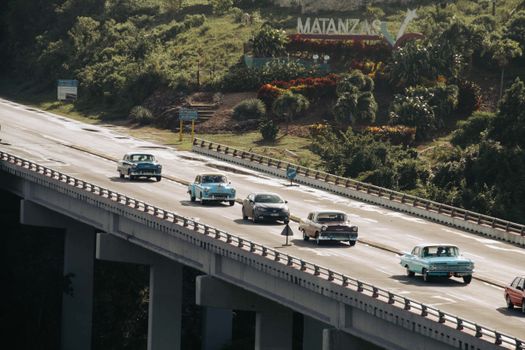 Classic cars crossing a bridge in Matanzas, Cuba, amidst lush greenery.