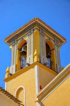 Low angle shot of a vibrant yellow church bell tower in Cehegín, Spain.