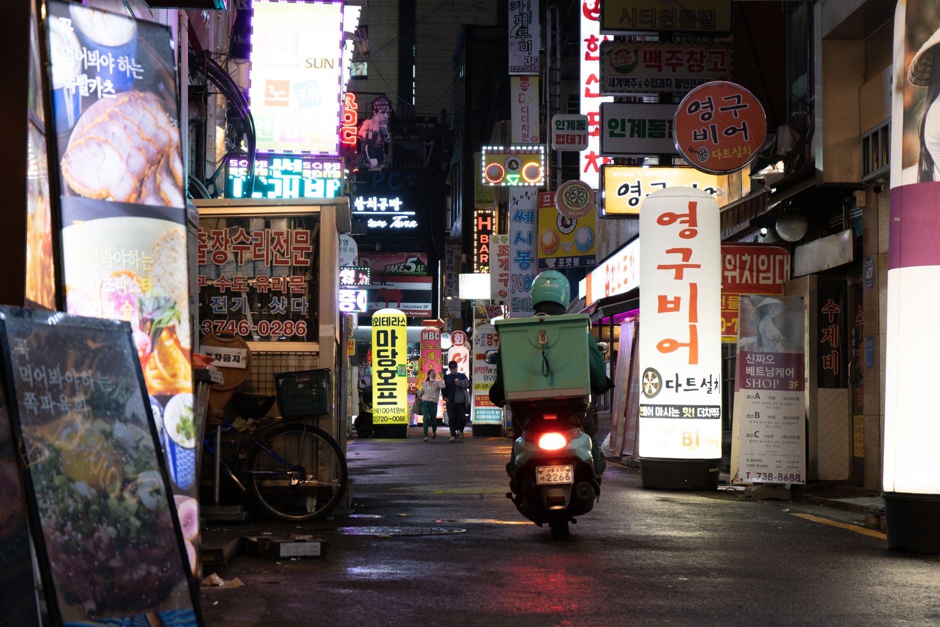 A bustling city street at night with neon lights and a delivery scooter navigating through.
