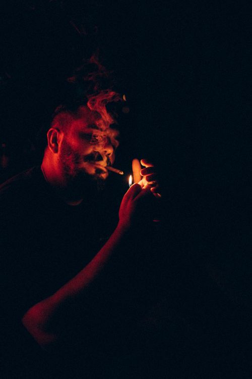 Free A dramatic and artistic portrait of a man lighting a cigarette against a dark background. Stock Photo