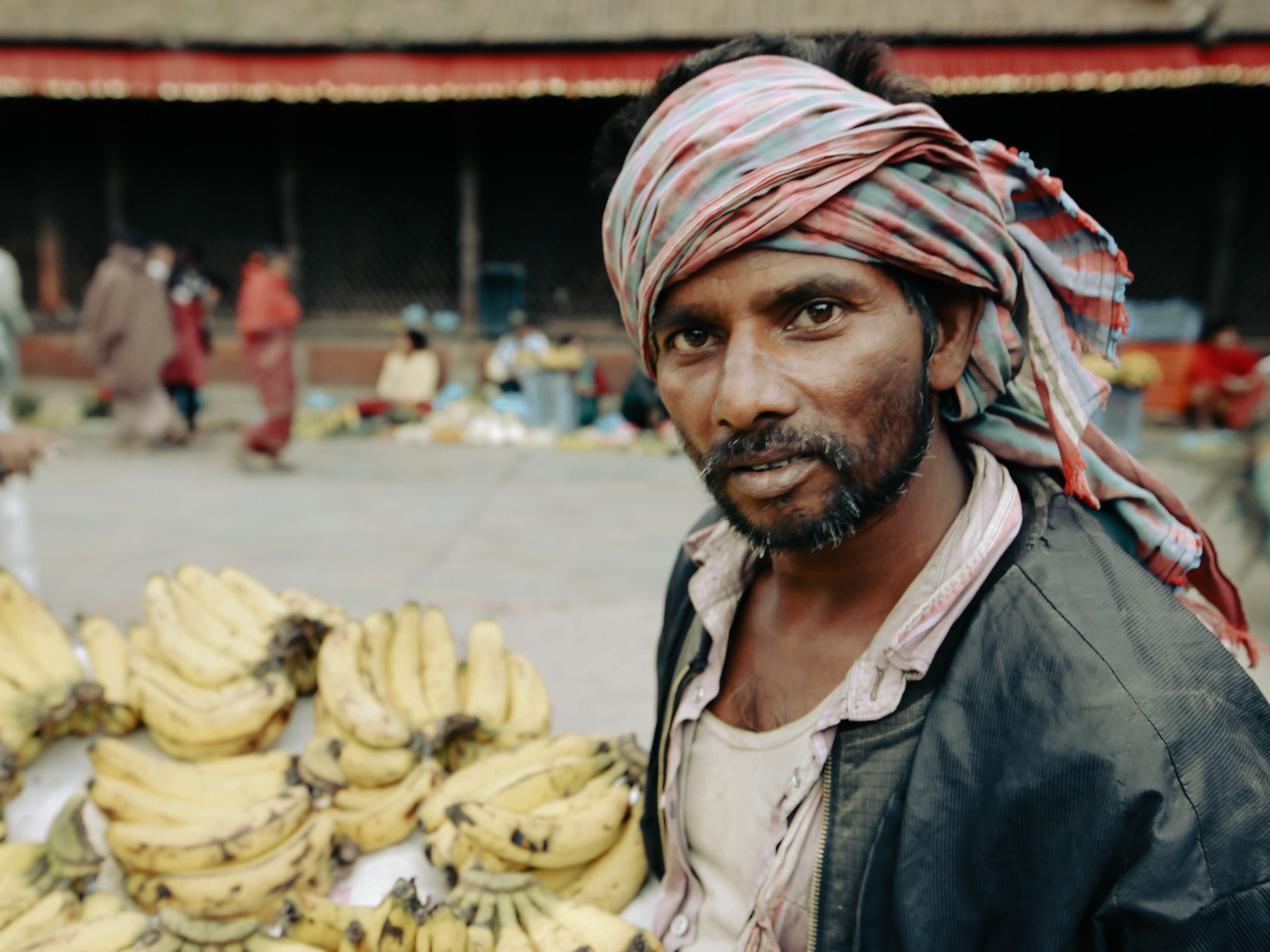 Portrait of a street vendor selling bananas at a bustling outdoor market with colorful background.