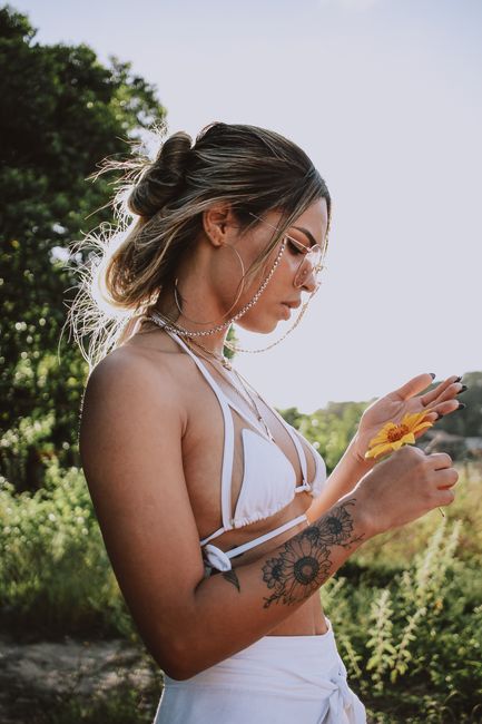 Profile view of a woman in a bikini holding a flower outdoors.