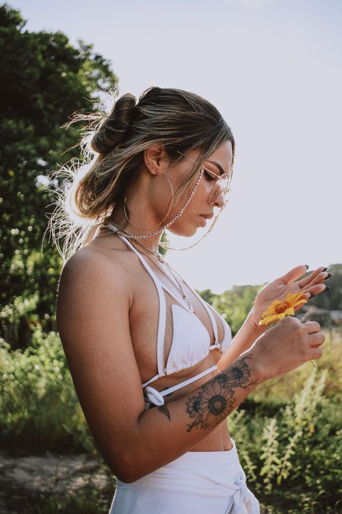 Free Profile view of a woman in a bikini holding a flower outdoors. Stock Photo