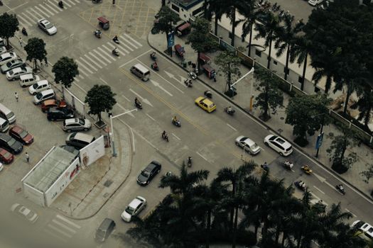 Aerial drone shot of a busy urban intersection with cars and scooters during the day.