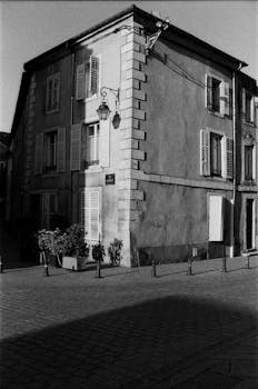 Grayscale photo of a classic European building corner with shutters and street lamp.