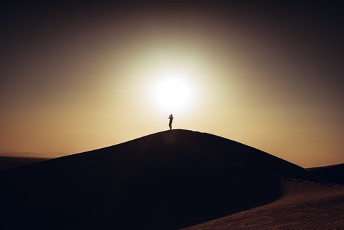 Free A striking silhouette of a person standing on a desert dune at sunset, reflecting solitude and nature's vastness. Stock Photo