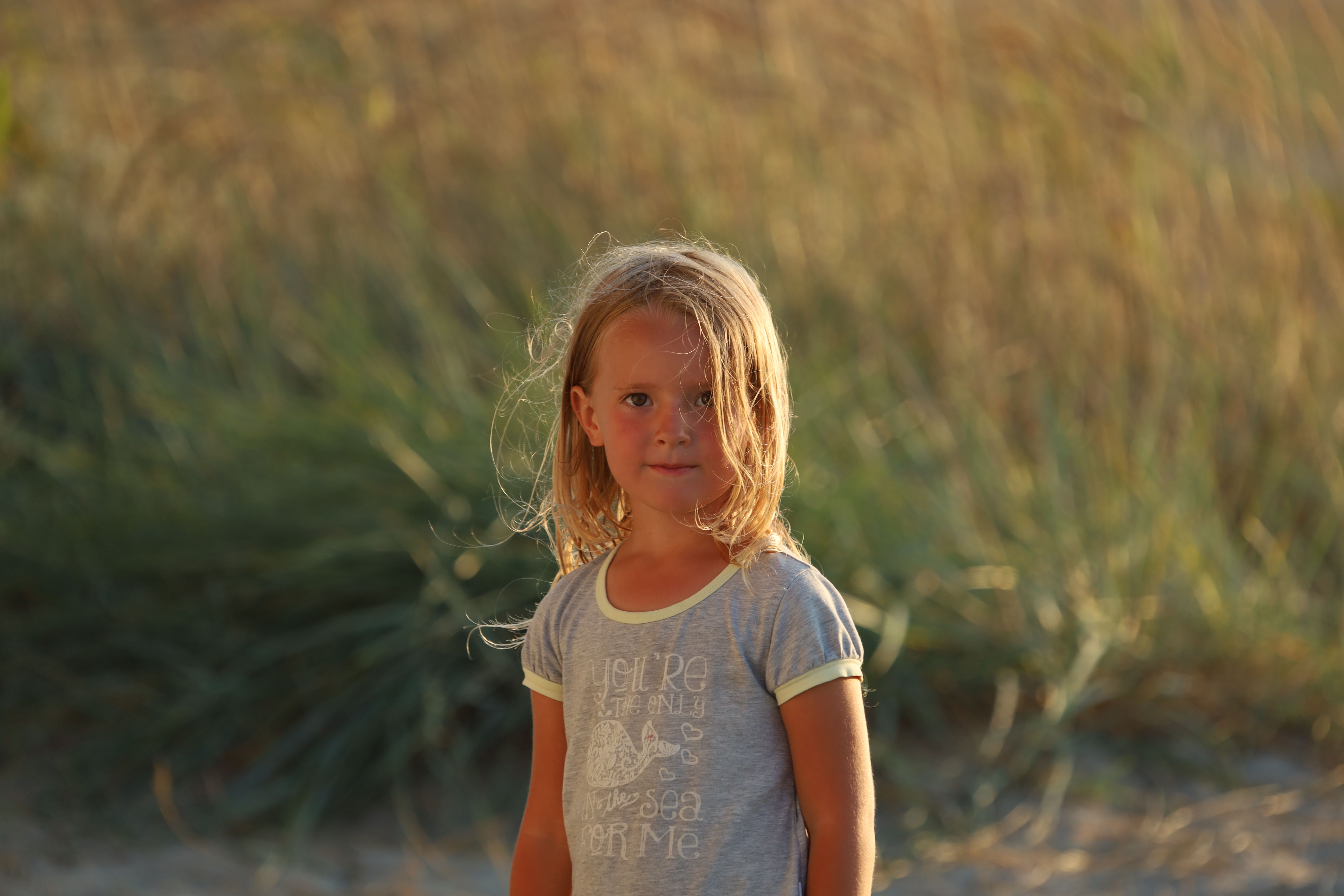 Portrait of a young girl in a gray shirt standing outdoors in warm evening light.