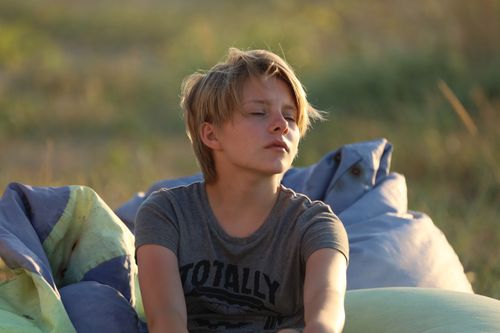 Free Blonde child sitting outdoors with closed eyes on a sunny day, enjoying nature. Stock Photo