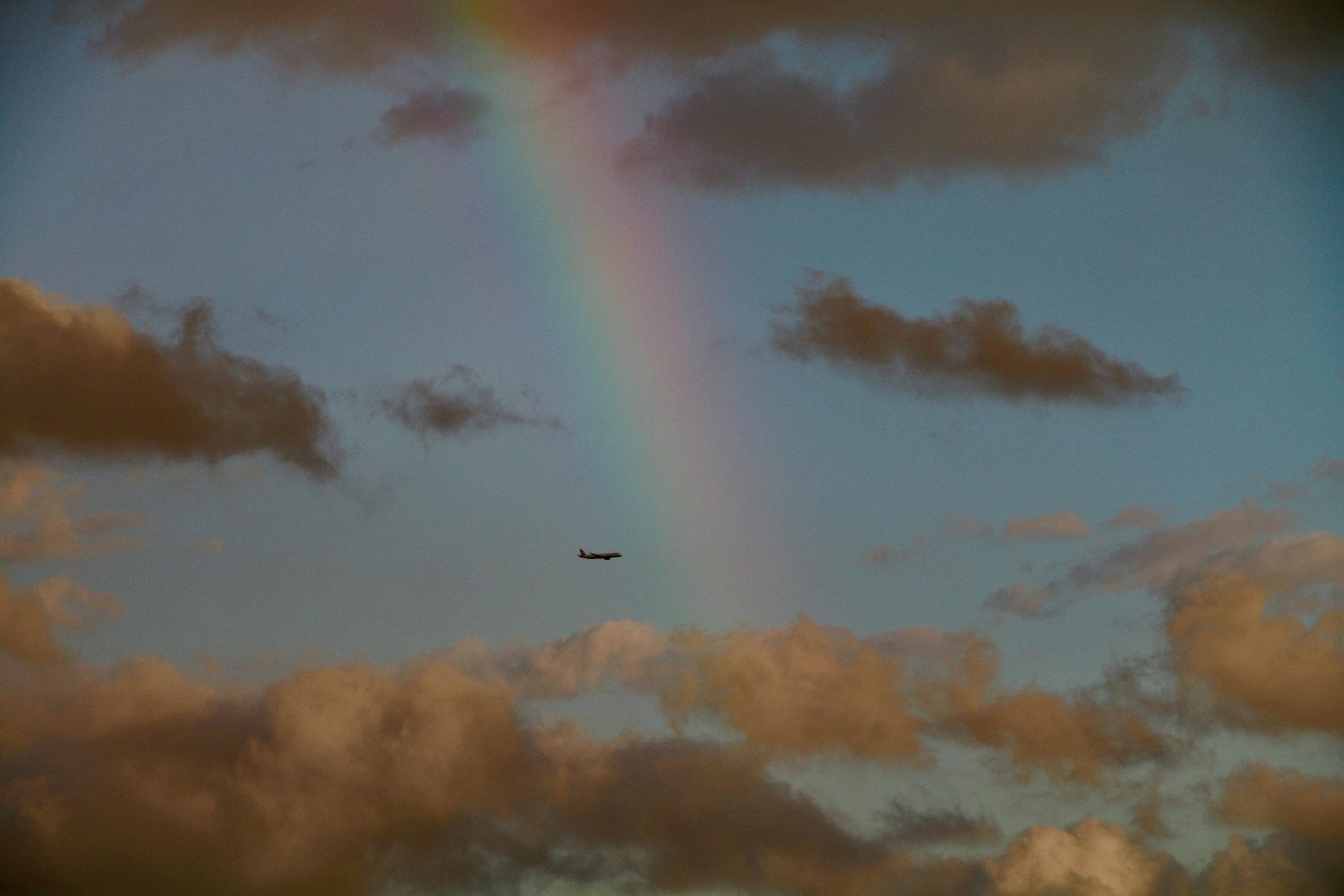 A majestic airplane flies beneath a colorful rainbow in a cloudy sky, capturing a unique travel moment.