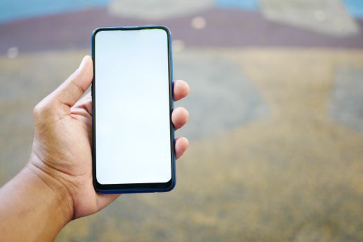 A close-up of a hand holding a smartphone with a blank white screen, outdoors.