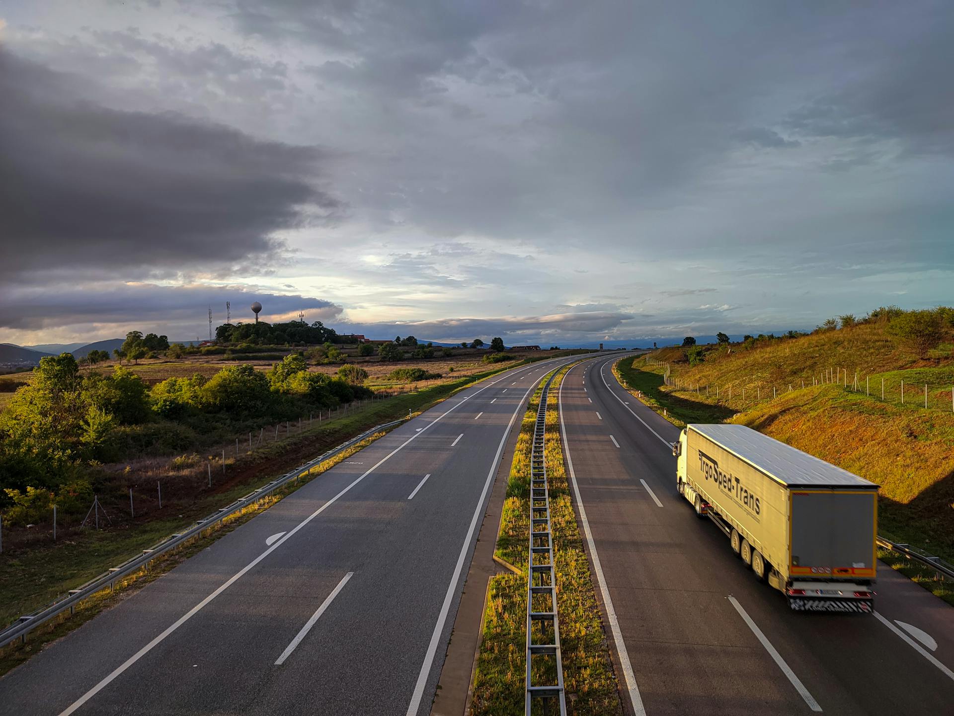 A scenic highway under a dramatic cloudy sky with a lone truck driving on an open road.