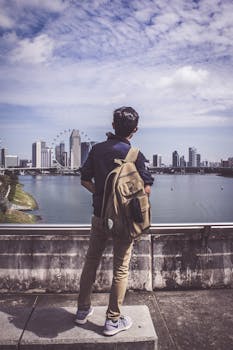 一名男子站在观景台上，在蓝天下凝望着河对岸的新加坡天际线