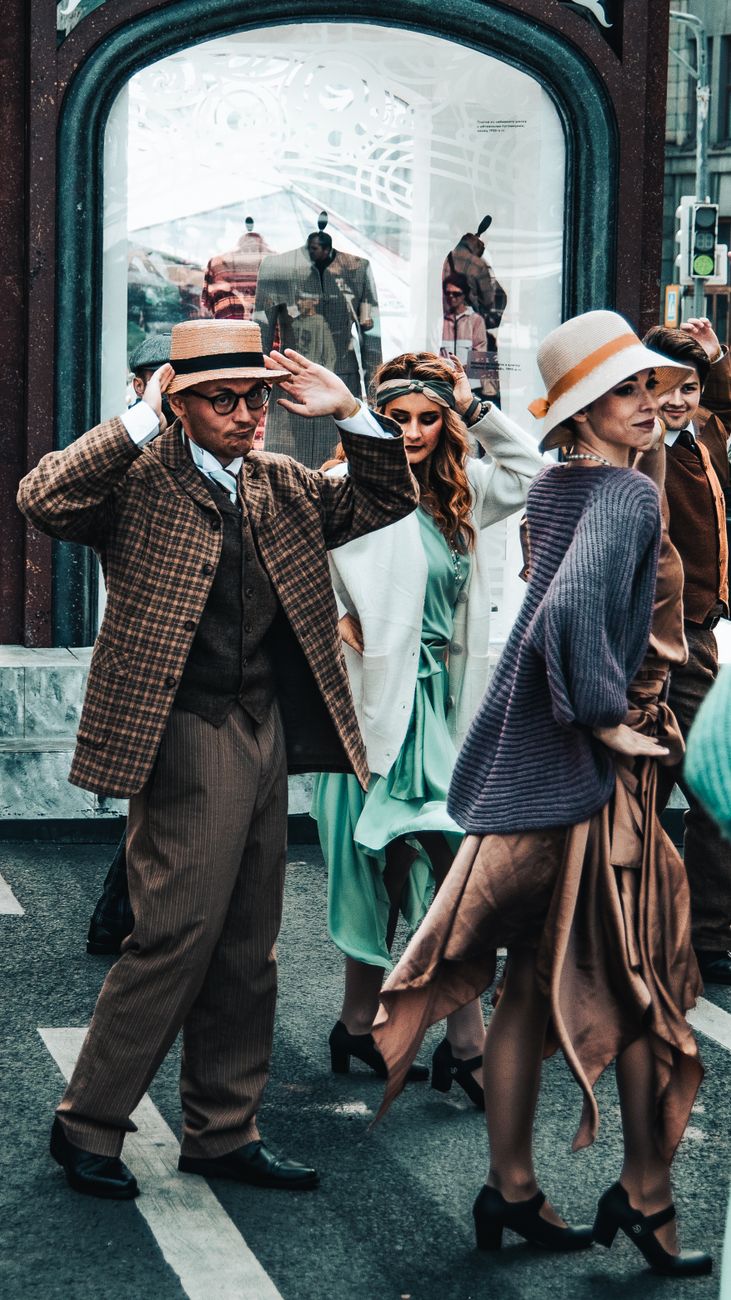 Stylish individuals in vintage outfits participate in a lively street parade.