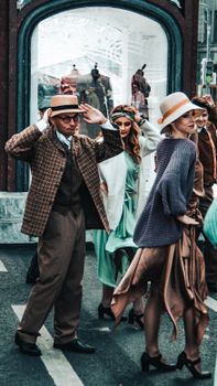 Stylish individuals in vintage outfits participate in a lively street parade.