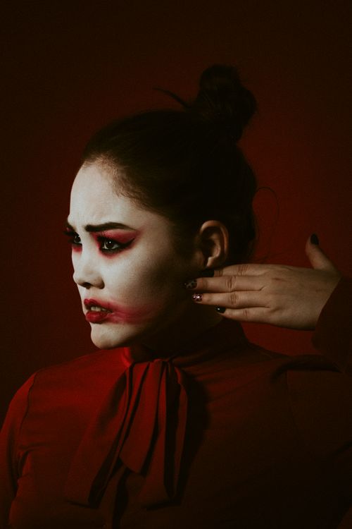 Free Striking portrait of a woman with bold, artistic makeup against a red background. Stock Photo
