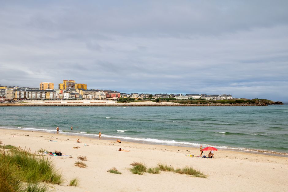 Día de verano relajante en la playa en Foz, Galicia, España, con olas del océano y pueblo costero.