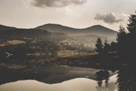 白天，薄雾笼罩下，湖面倒映着山景，天空多云