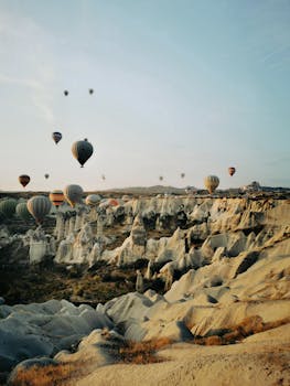 Stunning view of hot air balloons flying over Cappadocia's unique rock formations at sunrise.