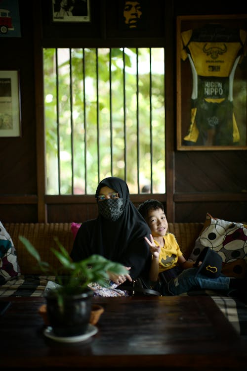 A Boy Sitting Beside a Person Wearing Black Hijab