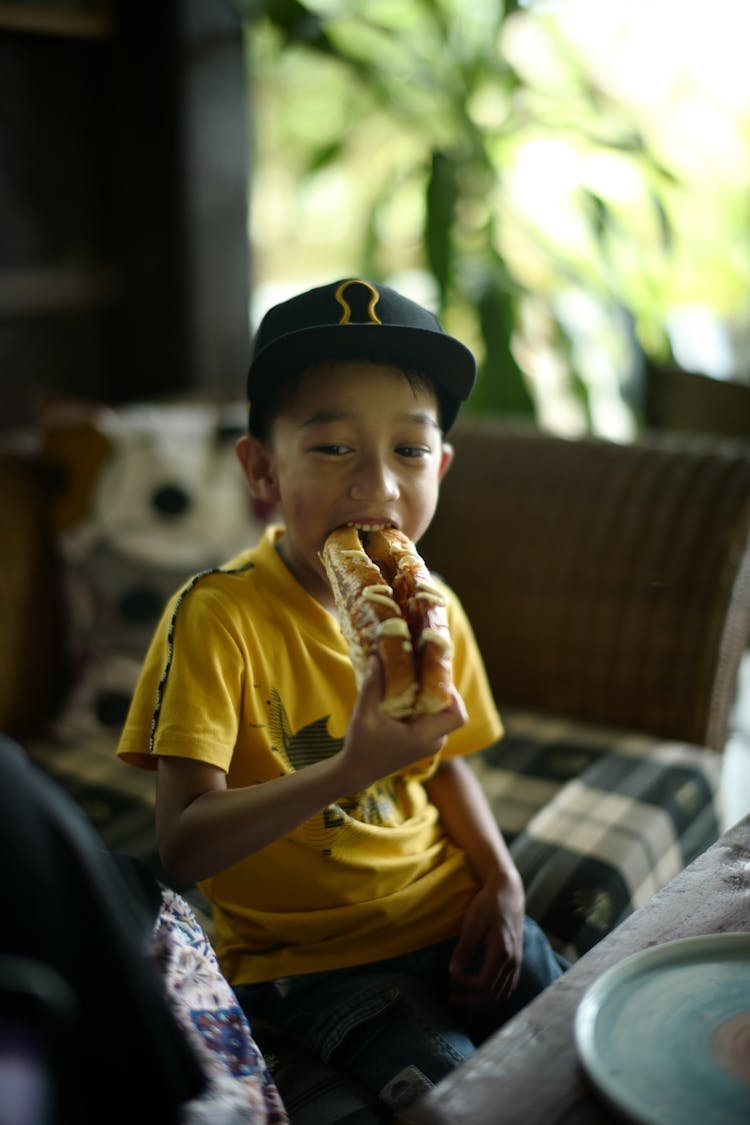 A Boy In Yellow Shirt Eating A Hotdog