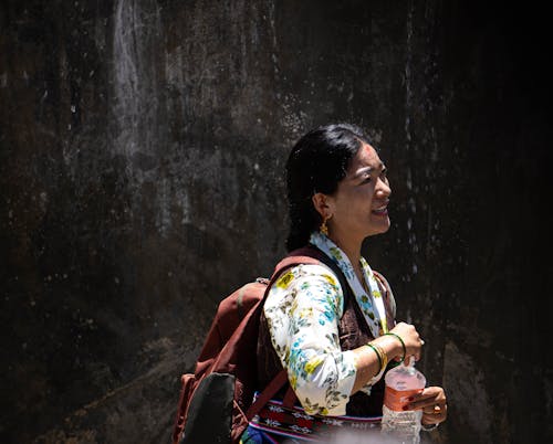 A Woman in Floral Long Sleeves Carrying Backpack while Opening a Bottled Water