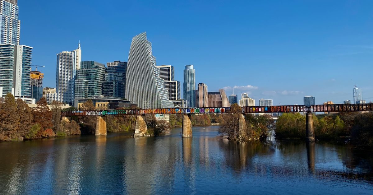 A stunning view of Austin's skyline with a bridge over the Colorado River under a clear blue sky.