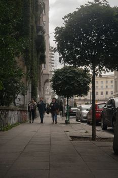 City street with people walking, green trees, and parked cars. Ideal for urban lifestyle concepts.