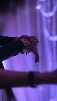 Close-up of hands with silver bangles and manicured nails, set against a purple backdrop.