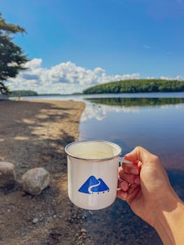 A tranquil lakeside scene in Jakes Landing, Canada with a hand holding a coffee mug.