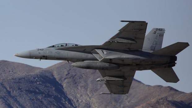 Military aircraft flying over mountainous terrain with clear blue skies.