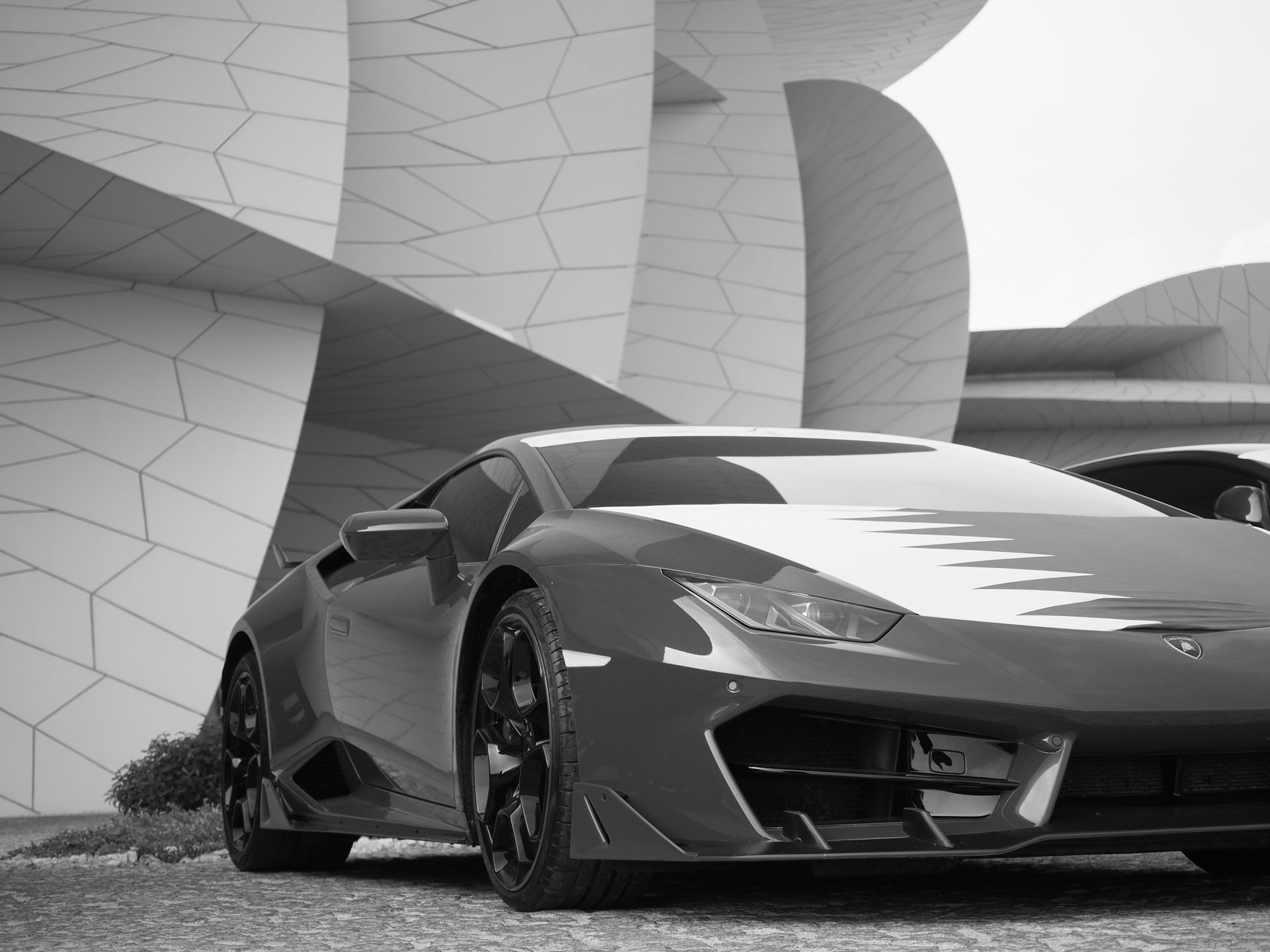 Black and white photo of a luxury sports car in front of Doha's contemporary architecture.