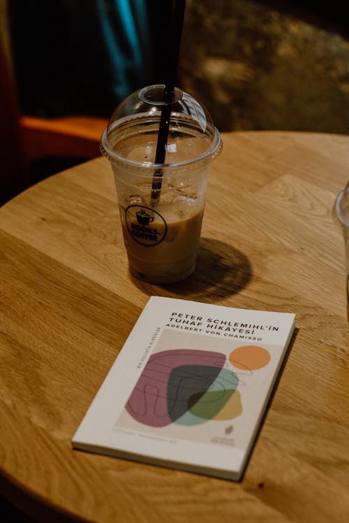 Clear Plastic Cup With Iced Coffee and Book on Wooden Table