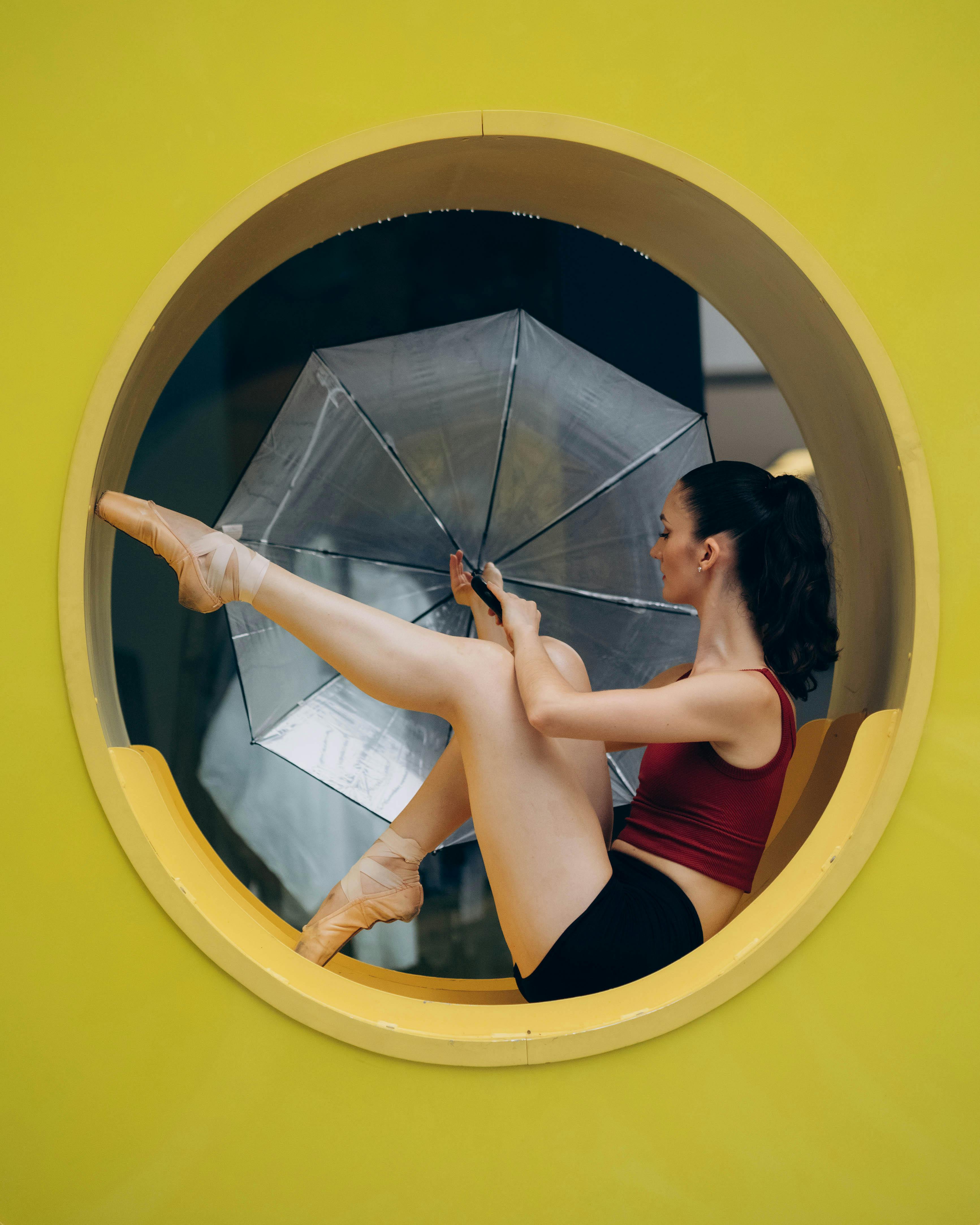 Artistic ballet dancer poses gracefully with umbrella in a vibrant yellow circular frame.