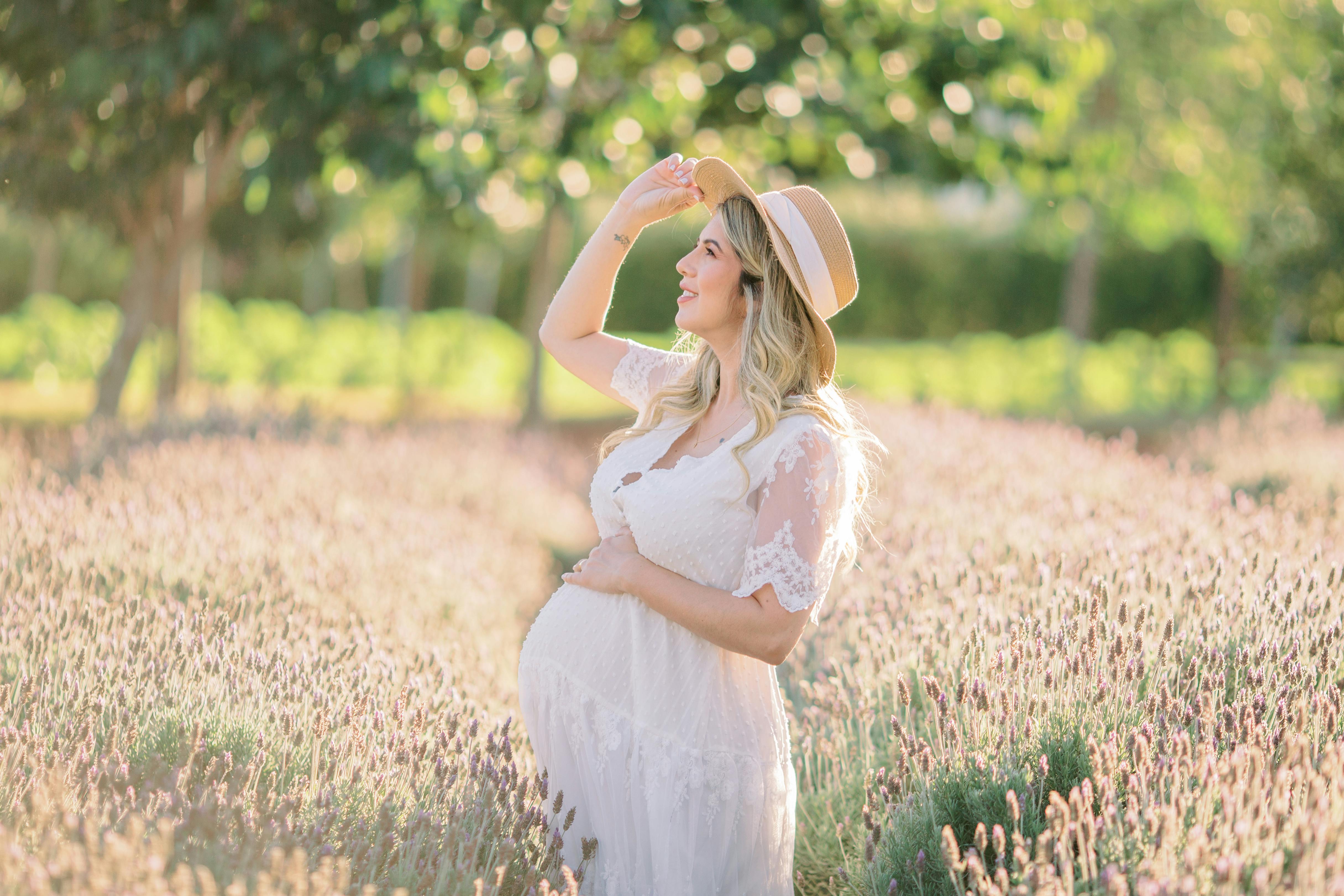 a pregnant woman in white dress wearing sun hat while looking afar