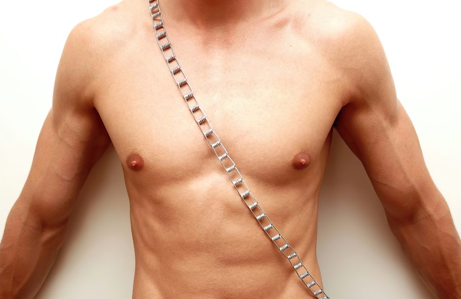 Close-up of a muscular male torso adorned with a stylish chain against a white background.