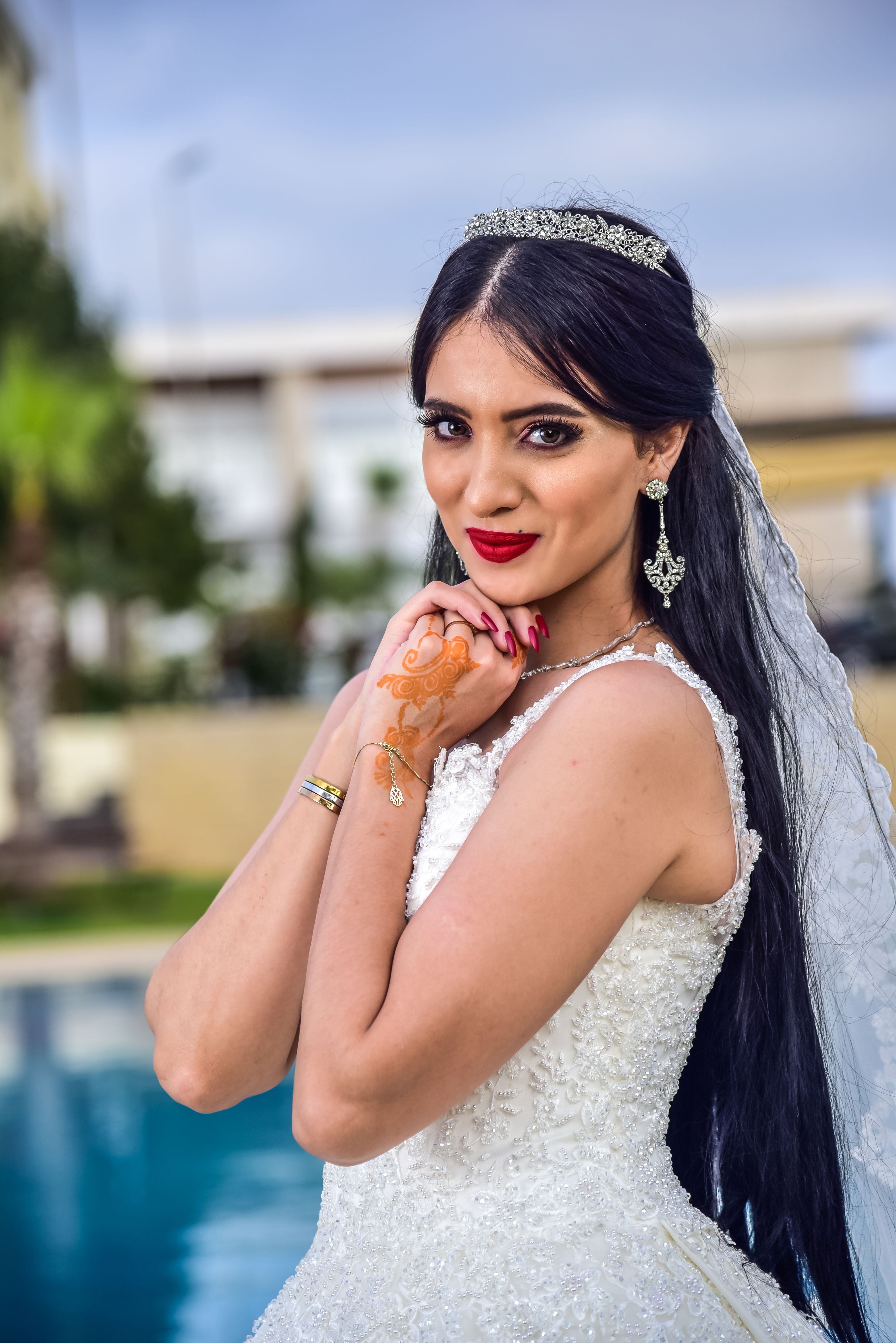 Beautiful South Asian bride in a lace wedding gown with henna tattoo and tiara posing outdoors.