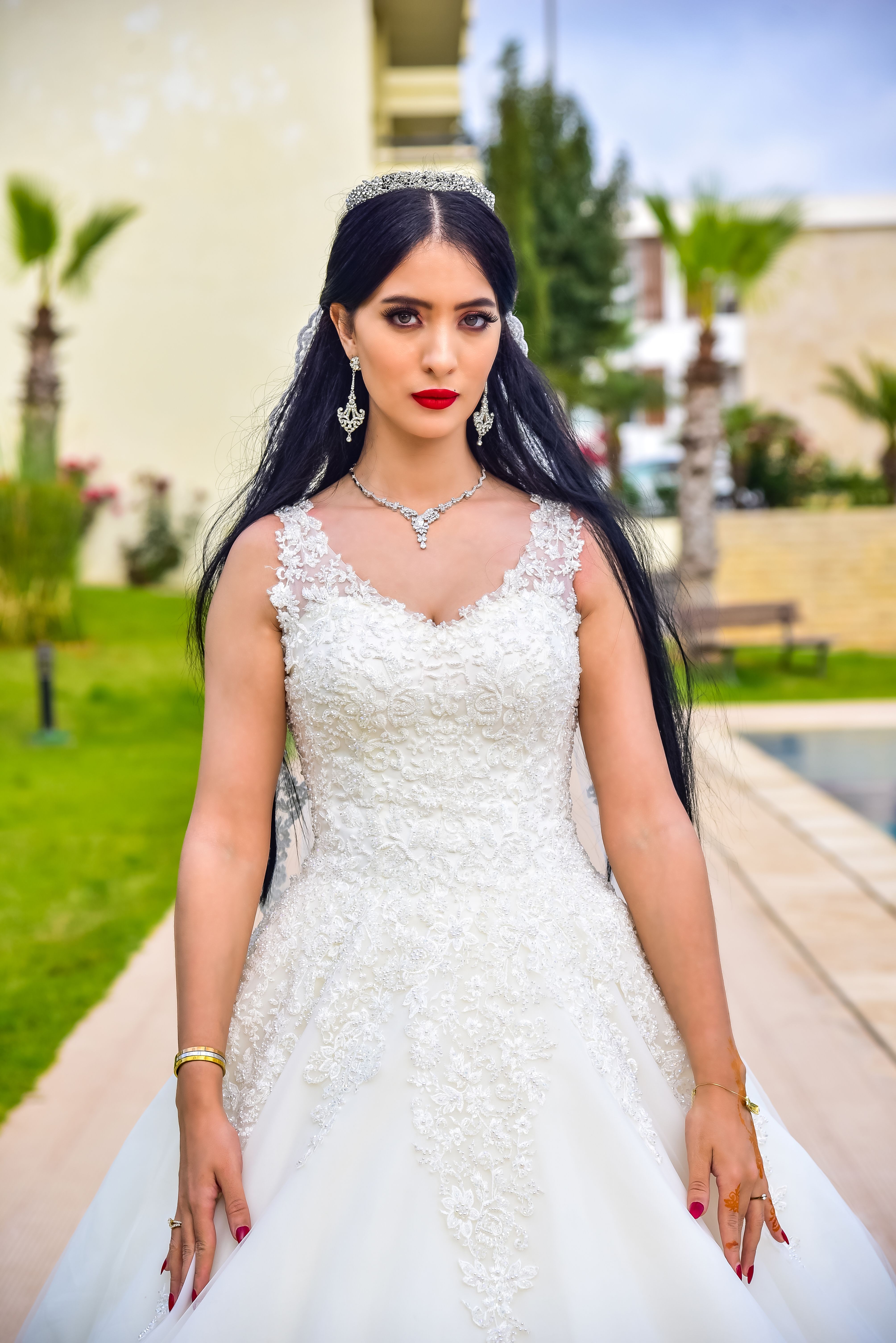 Stunning bride in a white wedding dress, posing outdoors with vivid greenery in the background.