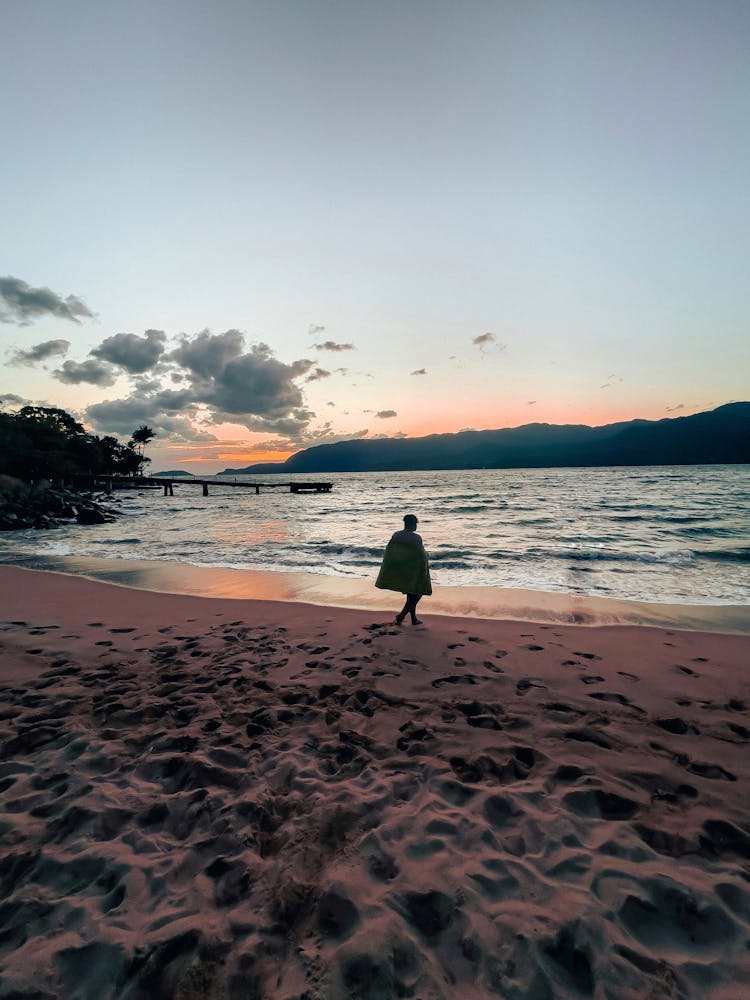 Man Walking On Beach On Sunset