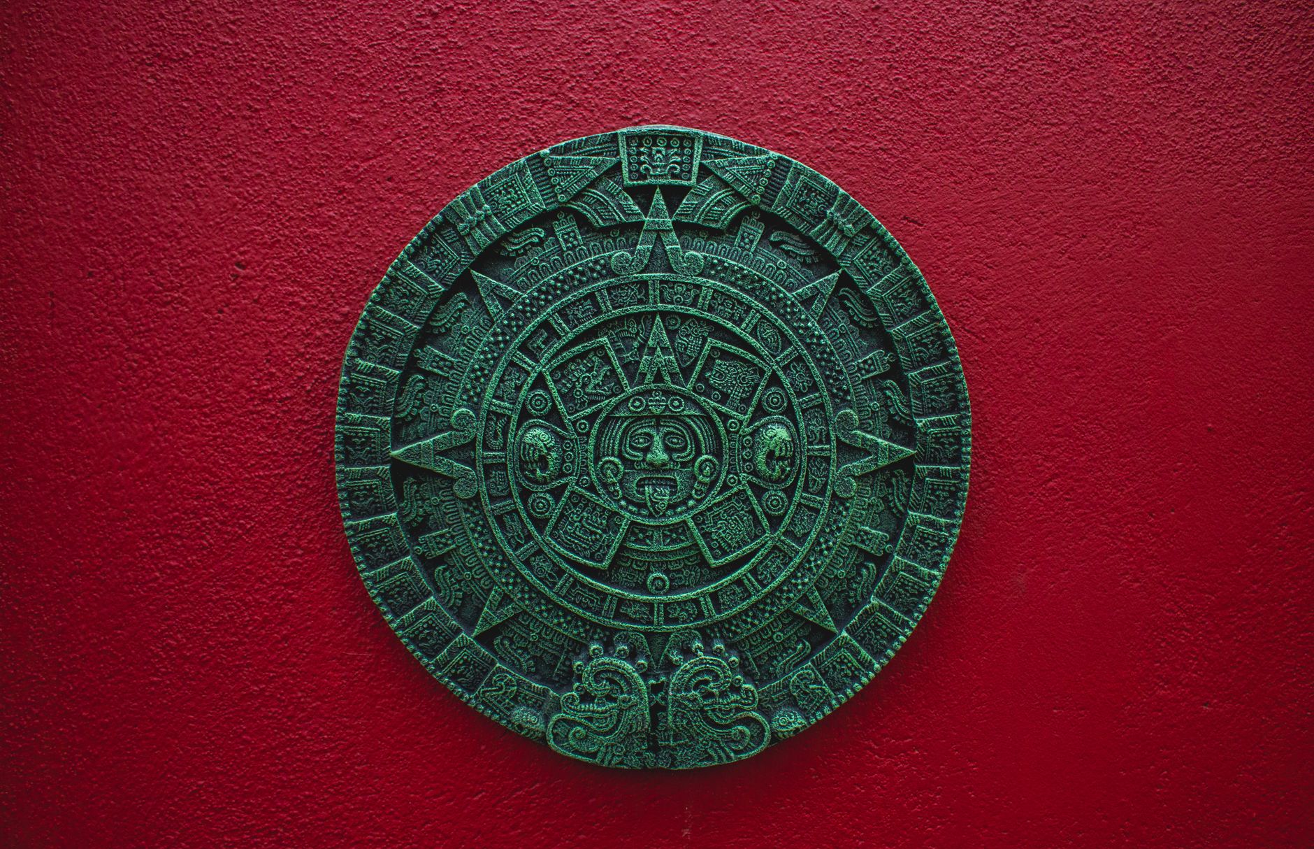 Mayan calendar decor on a vibrant red wall, symbolizing ancient Mexican culture.
