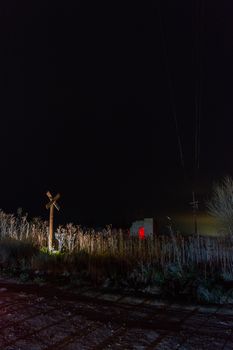A dimly lit railroad crossing at night with a red illuminated sign nearby.