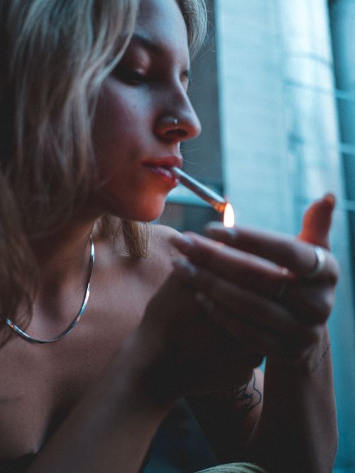 Free A woman relaxes while lighting a cigarette, capturing a contemplative moment. Stock Photo