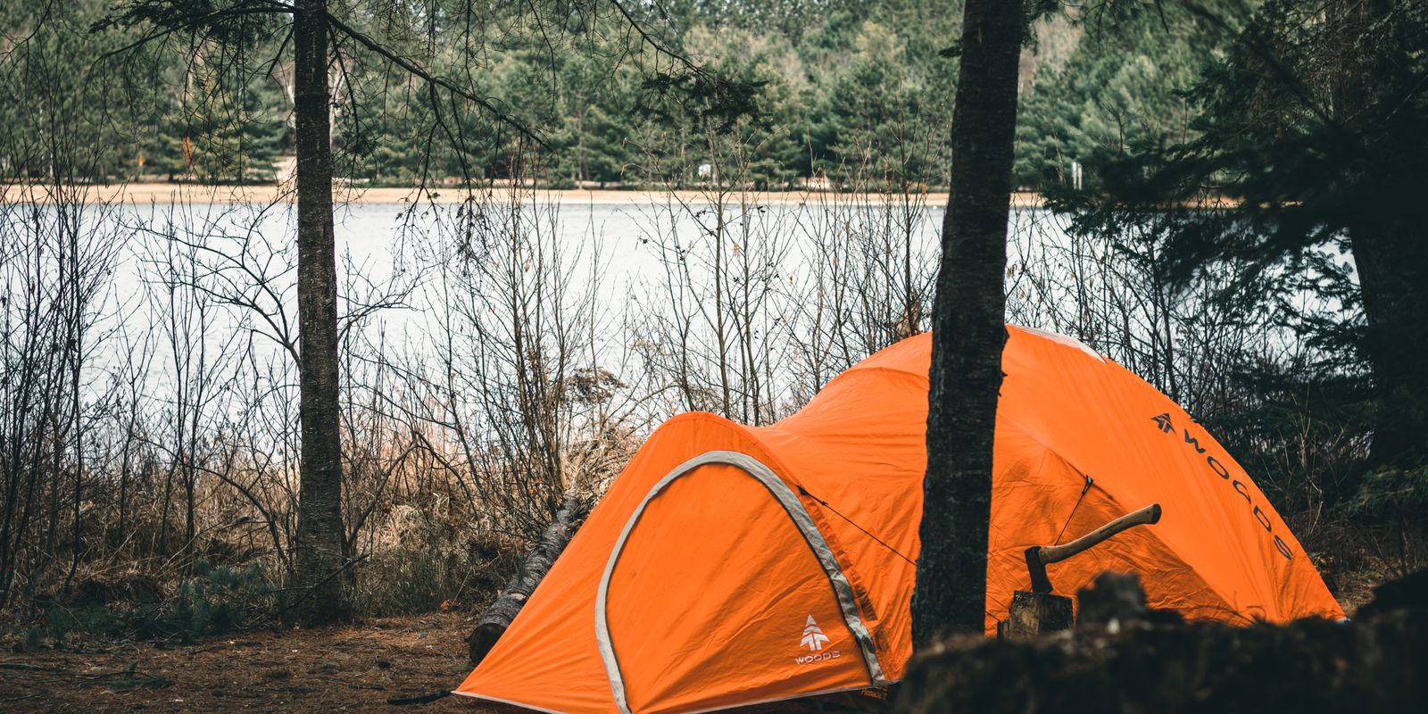 An orange tent pitched near a serene lake surrounded by trees
