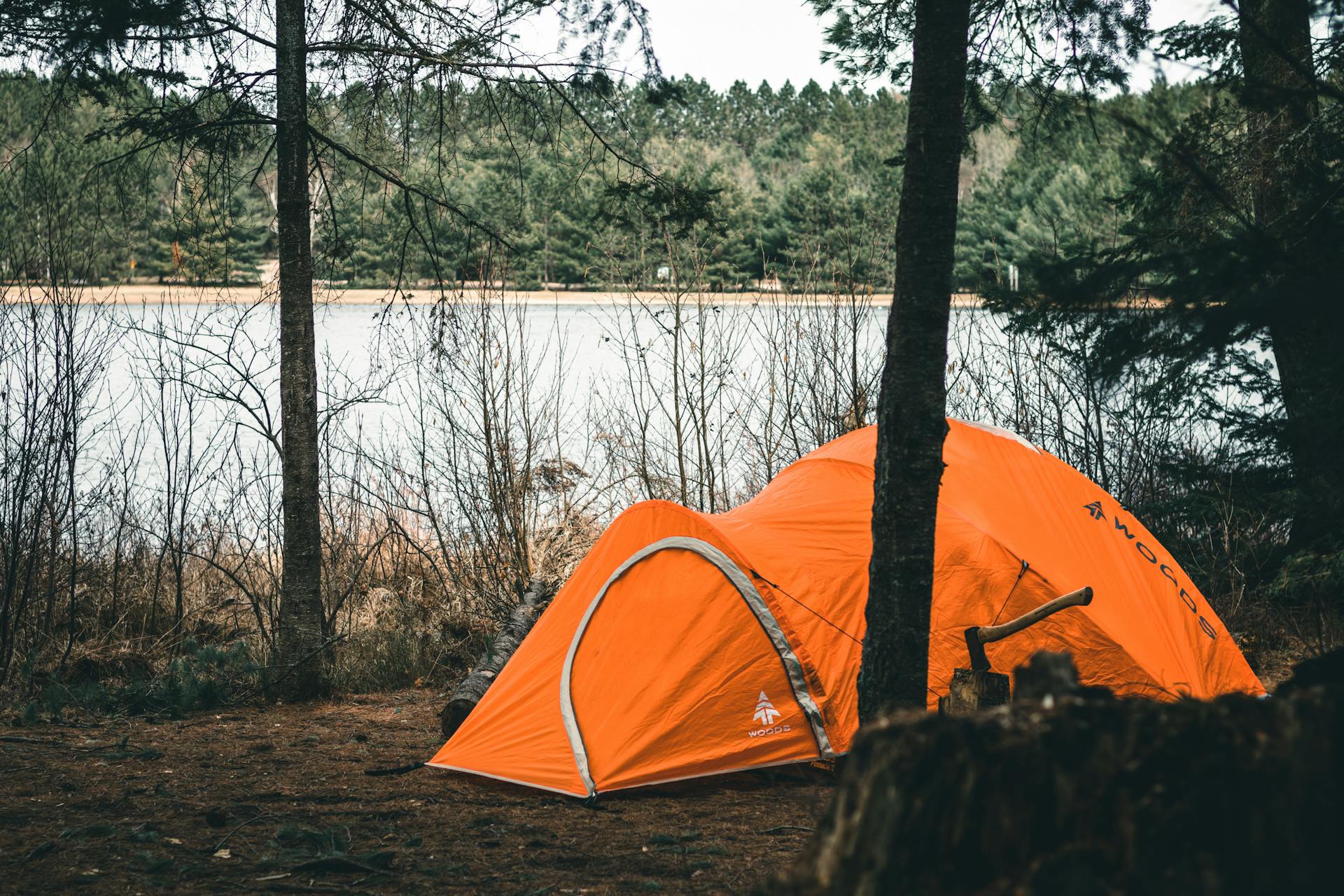 Orange tent pitched near a serene lake in Algonquin Park, surrounded by trees.