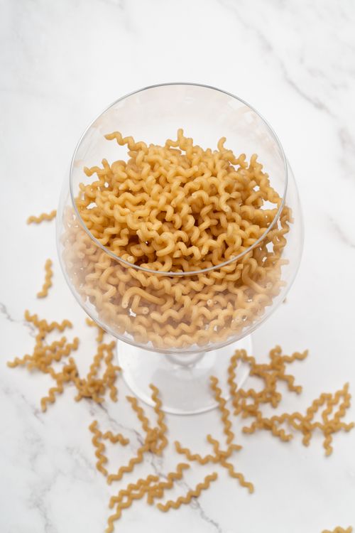 Free Close-up of cavatappi pasta in a wine glass on a marble surface, showcasing food art. Stock Photo