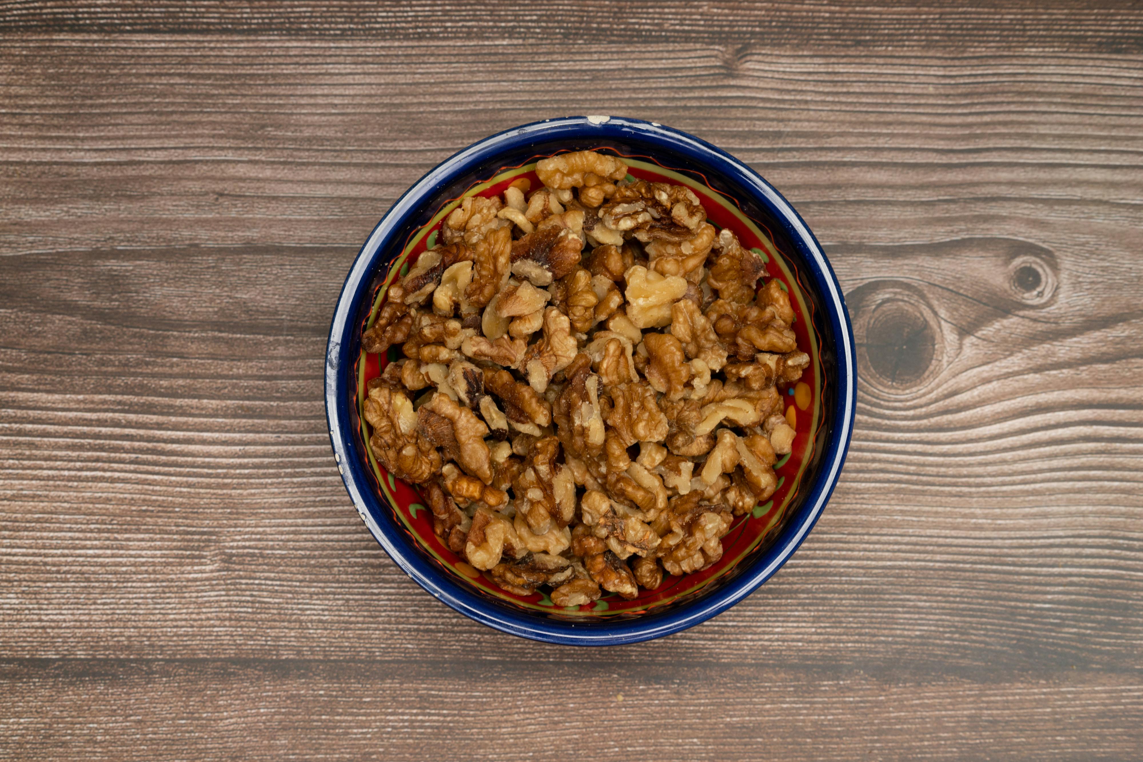 A vibrant top-view image of shelled walnuts in a colorful decorative bowl on a wooden surface.