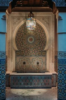 Elegant Moroccan-style mosaic tile fountain with ornate geometric patterns and a hanging lantern, perfect for interior design inspiration.