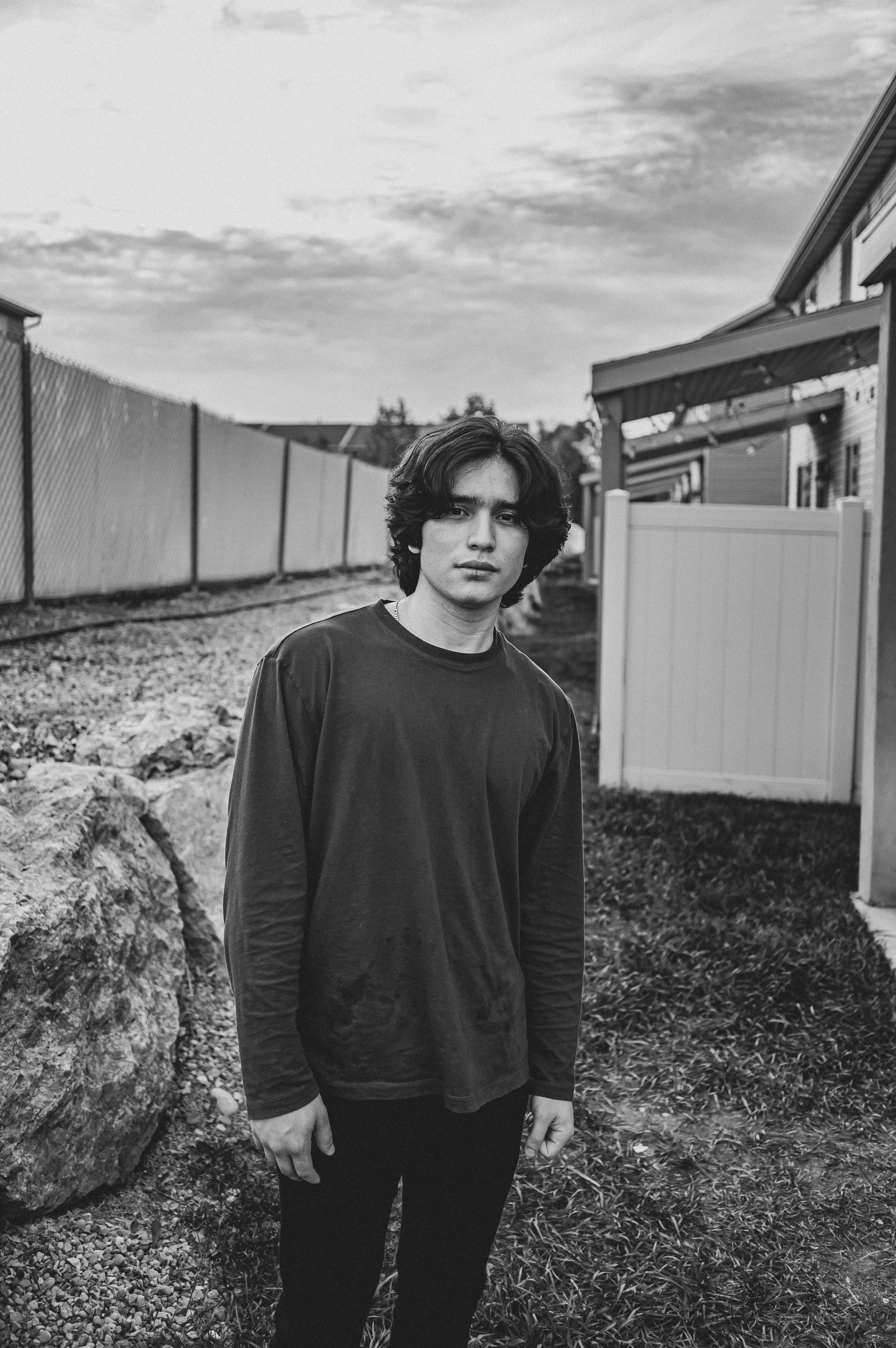 Black and white portrait of a young man standing outdoors, showcasing contemplative mood.